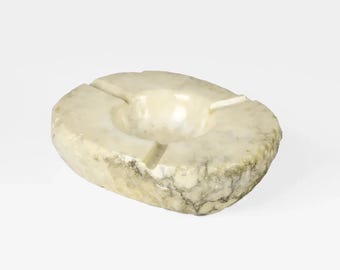 Pode incluir: Um cinzeiro de mármore branco com uma forma arredondada e orgânica. O cinzeiro tem três reentrâncias para cigarros.
