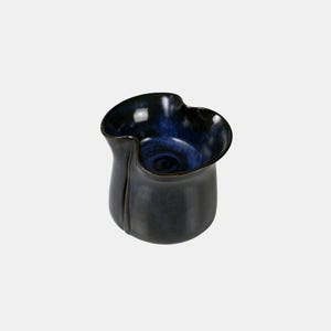 May include: A dark blue ceramic vase with a contrasting deep blue interior. The vase has an organic shape with a ruffled rim and a vertical groove detail. The glossy finish enhances the colour variations. The vase is suitable for displaying flowers.