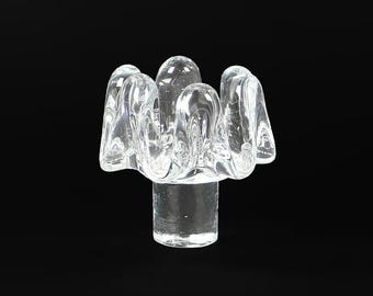 May include: A clear glass decorative object with a unique, organic shape. The object features a cylindrical base supporting a cluster of rounded, petal-like forms. The glass is transparent, allowing light to pass through, and is set against a black background.