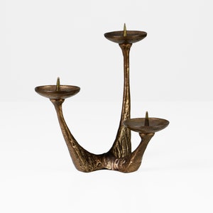 May include: A three-armed bronze candlestick with a textured finish. Each arm has a circular candle holder with a small, pointed brass finial.