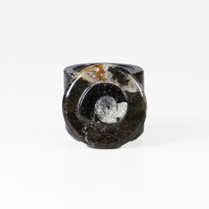 May include: A dark, patterned ring with a circular design. The ring features a mix of black, brown, and white colors, with a polished finish. The ring is a unique piece of jewelry.