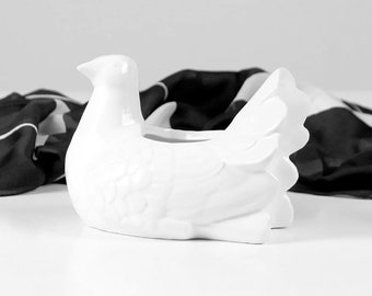 May include: White ceramic dove shaped planter. The dove is sitting on a black fabric background.