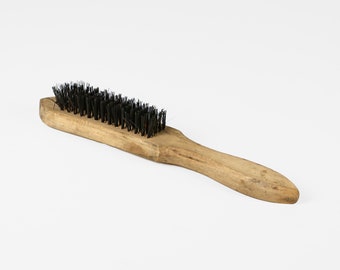 May include: A wooden-handled brush with black wire bristles. The brush is made of natural wood and has a simple design.