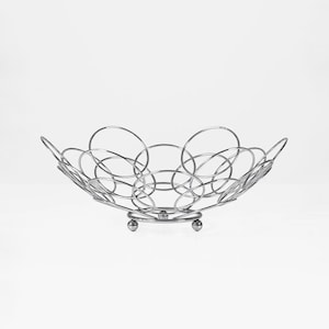 Könnte beinhalten: Eine moderne, silberfarbene Obstschale. Die Schale besteht aus miteinander verbundenen kreisförmigen Metallringen, die ein dekoratives, offenes Design bilden. Sie steht auf einem kleinen, kreisförmigen Sockel, der von drei kugelförmigen Füßen getragen wird. Die Schale ist breit und flach.