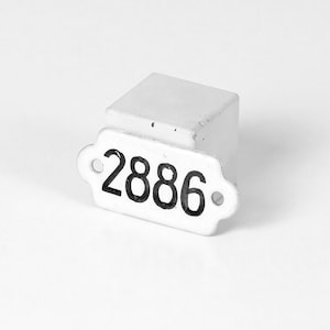Könnte beinhalten: Weißer Keramik-Anhänger mit schwarzen Zahlen "2886" auf weißem Hintergrund.