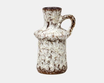 May include: A ceramic vase with a handle, featuring a textured, speckled design in shades of brown and white. The vase has a bulbous midsection and a narrow neck, with a dark brown rim and handle. This decorative piece is suitable for home decor.
