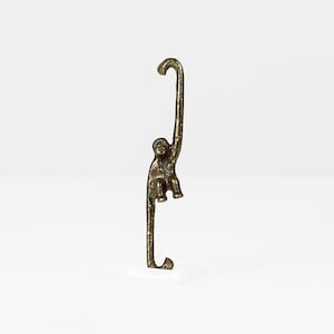 May include: A gold monkey figurine hanging from a hook. The monkey is sitting with its legs dangling and its tail curled around the hook.