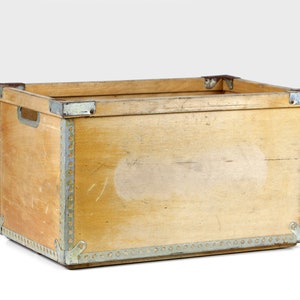 May include: A wooden storage box with metal trim and a light brown finish. The box has a rectangular shape and is made of wood with metal accents.