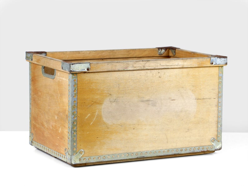 May include: A wooden storage box with metal trim and a light brown finish. The box has a rectangular shape and is made of wood with metal accents.