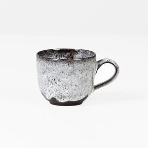 Può includere: Una tazza in ceramica bianca con una glassa marrone macchiata. La tazza ha una forma arrotondata e un manico.