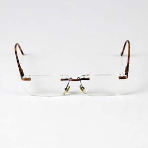 May include: A pair of rimless eyeglasses with a brown metal frame and clear lenses.