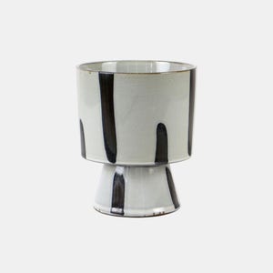 Könnte beinhalten: Ein Keramik-Pflanzgefäß mit Sockel. Der cremefarbene Pflanztopf hat vertikale schwarze Streifen. Der Innenraum ist sichtbar, und der Rand hat ein natürliches, unglasiertes Aussehen. Der Pflanztopf ist für Zimmerpflanzen geeignet.