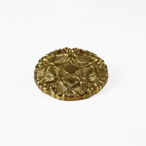 Puede incluir: Un botón redondo de metal dorado con un intrincado diseño floral.