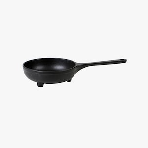 May include: A small, black cast iron skillet with a long handle and three small feet. The pan is round with a deep bowl shape, perfect for individual servings or small dishes. The handle has a hole for hanging.