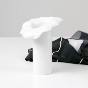 May include: White ceramic vase with a unique flower-shaped opening. The vase is cylindrical and has a smooth, glossy finish.