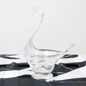 Puede incluir: Un cuenco de vidrio transparente en forma de cisne con un diseño de remolino. El cuenco está sobre una superficie rayada en blanco y negro.