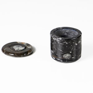 May include: A black and white marble ashtray and a matching lid. The ashtray is cylindrical with a circular opening. The lid is a flat, round disc. The marble has a natural pattern of swirls and specks.