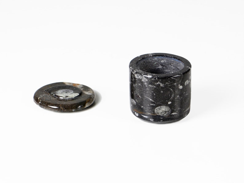 May include: A black and white marble ashtray and a matching lid. The ashtray is cylindrical with a circular opening. The lid is a flat, round disc. The marble has a natural pattern of swirls and specks.