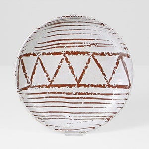 May include: A white ceramic plate with a brown geometric design. The design features a band of triangles and horizontal lines.