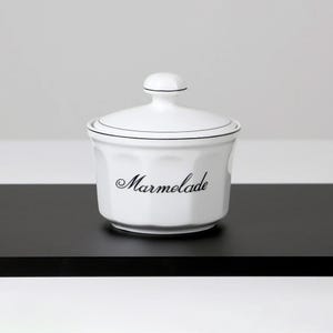 Peut inclure: Pot en céramique blanche avec un couvercle noir et une ligne noire autour du haut. Le pot porte l'inscription "Marmelade" en cursive noire sur le devant.