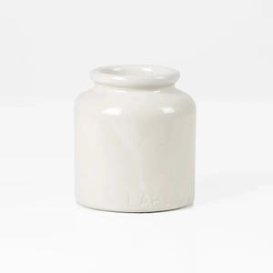 May include: A small, off-white ceramic jar with a rounded body and a slightly flared rim. The jar has a smooth, glossy finish and the word "TABLE" is embossed on the lower portion of the jar. The jar is likely used for storage or display.