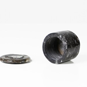 May include: A dark gray marble container with a matching lid. The cylindrical container is open at both ends and has a polished finish. The lid is a flat, circular piece. The items are set against a white background.