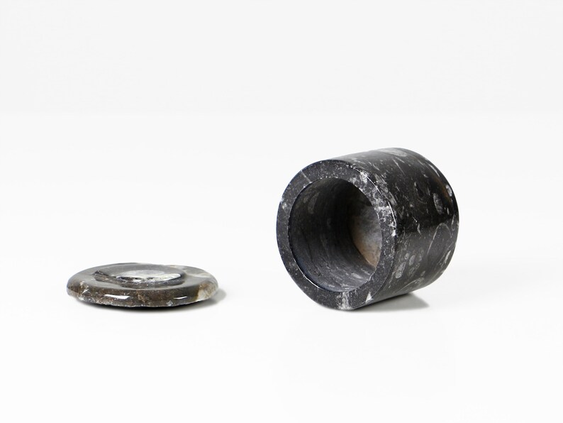 May include: A dark gray marble container with a matching lid. The cylindrical container is open at both ends and has a polished finish. The lid is a flat, circular piece. The items are set against a white background.
