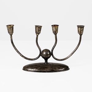 May include: A silver four-armed candelabra with a round base and a textured finish. The arms are curved and each has a small, round cup at the end.