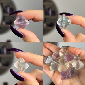 May include: A collection of fluorite crystals in various shades of purple, green, and clear. The crystals are octahedral in shape and have a glassy lustre.