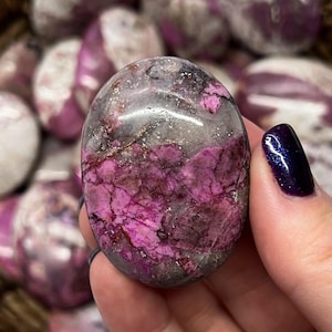 May include: A smooth, polished, pink and grey gemstone with a swirling pattern. The stone is a tumbled, oval shape.