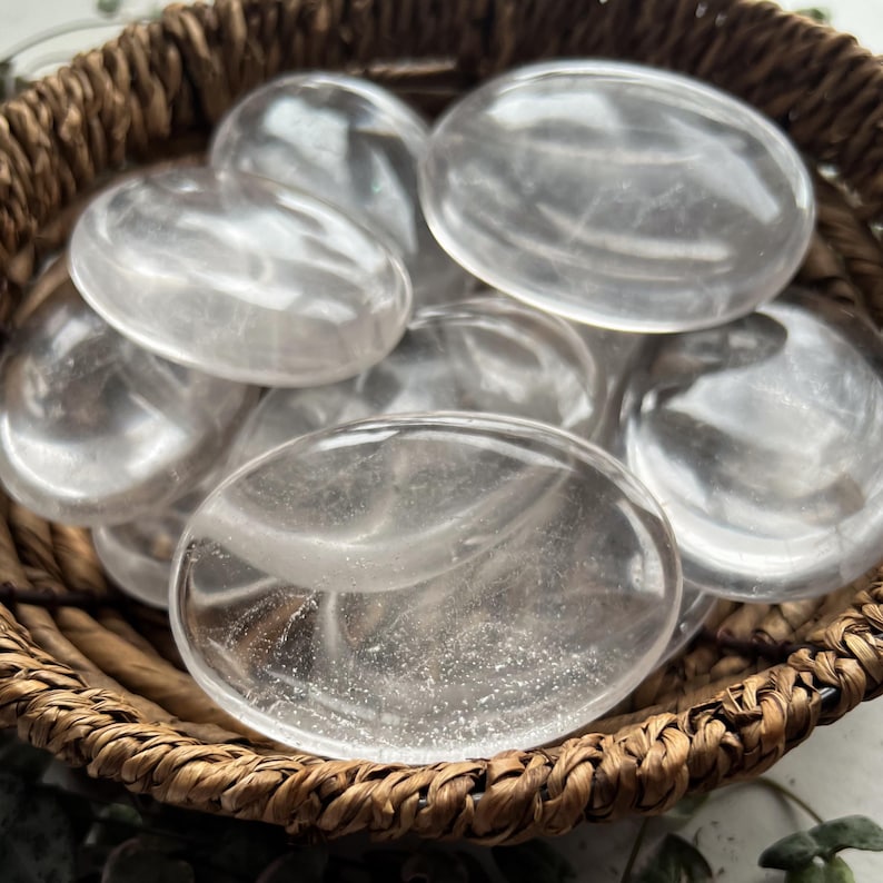 May include: A collection of clear quartz crystal points in a woven basket. The crystals are smooth and polished, with a slight sparkle.