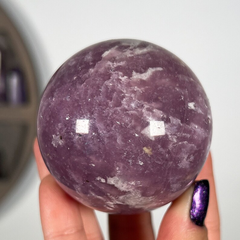 May include: A large, purple amethyst sphere with white swirls and inclusions. The sphere is smooth and polished.