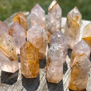 May include: A collection of 14 pink and orange crystal points. The points are all different sizes and shapes, and they have a variety of inclusions. The crystals are arranged in a random pattern on a wooden surface.