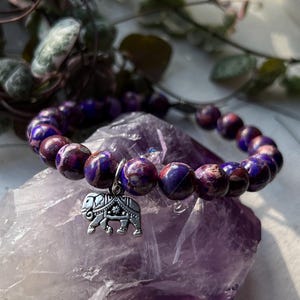 May include: Purple and white marbled stone beaded bracelet with a silver elephant charm.