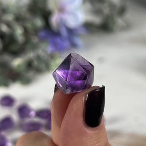 May include: A purple amethyst crystal shaped like a pyramid with multiple facets.