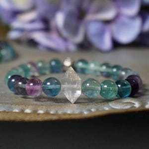 May include: A bracelet made of blue, green, and purple beads with a clear crystal charm in the center.