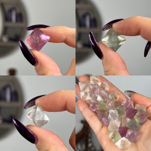 May include: A collection of fluorite crystals in various shades of pink, green, and purple. The crystals are octahedral in shape and have a glassy lustre.