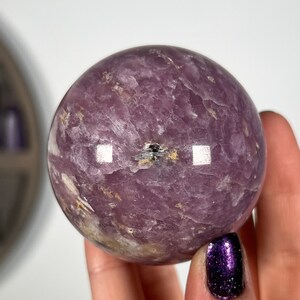 May include: A large, purple amethyst sphere with a swirling pattern and a small black inclusion in the center.