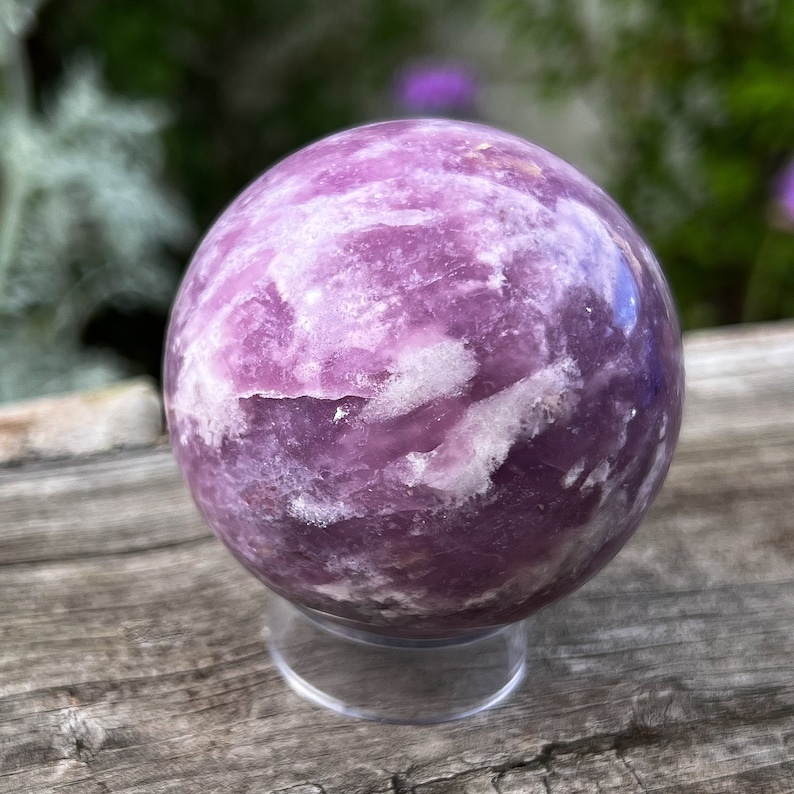 May include: A large, purple and white amethyst sphere on a clear stand. The sphere has a swirling, cloudy pattern.