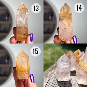 May include: Four clear quartz crystal points with inclusions of golden rutile and a hint of pink. The crystals are displayed on a wooden surface and in hands.