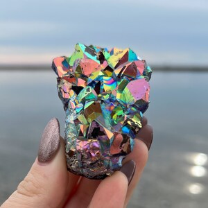 May include: A cluster of iridescent rainbow amethyst crystals with a variety of colors, including purple, green, blue, and gold. The crystals are arranged in a cluster and have a rough, natural texture.