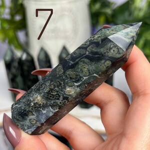 Pode incluir: Uma ponta de pedra verde e preta salpicada, tamb&eacute;m conhecida como varinha de cristal, com uma ponta pontiaguda. A pedra &eacute; segurada na m&atilde;o.
