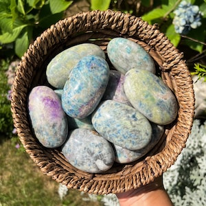 May include: A collection of smooth, oval-shaped blue, green, and white stones with a marbled pattern. The stones are in a woven basket.