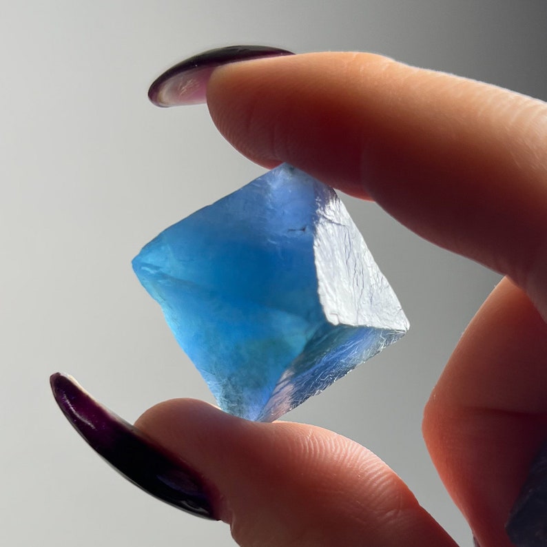 Puede incluir: Un cristal de fluorita azul en forma de cubo. El cristal es transl&uacute;cido y tiene un ligero brillo.