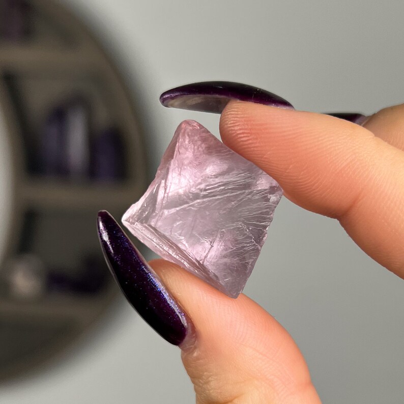 May include: A clear, pink fluorite crystal with a square shape and a smooth, polished surface.