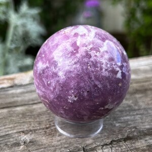 May include: A polished purple and white Lepidolite sphere on a clear stand. The sphere has a swirling pattern of white and purple.