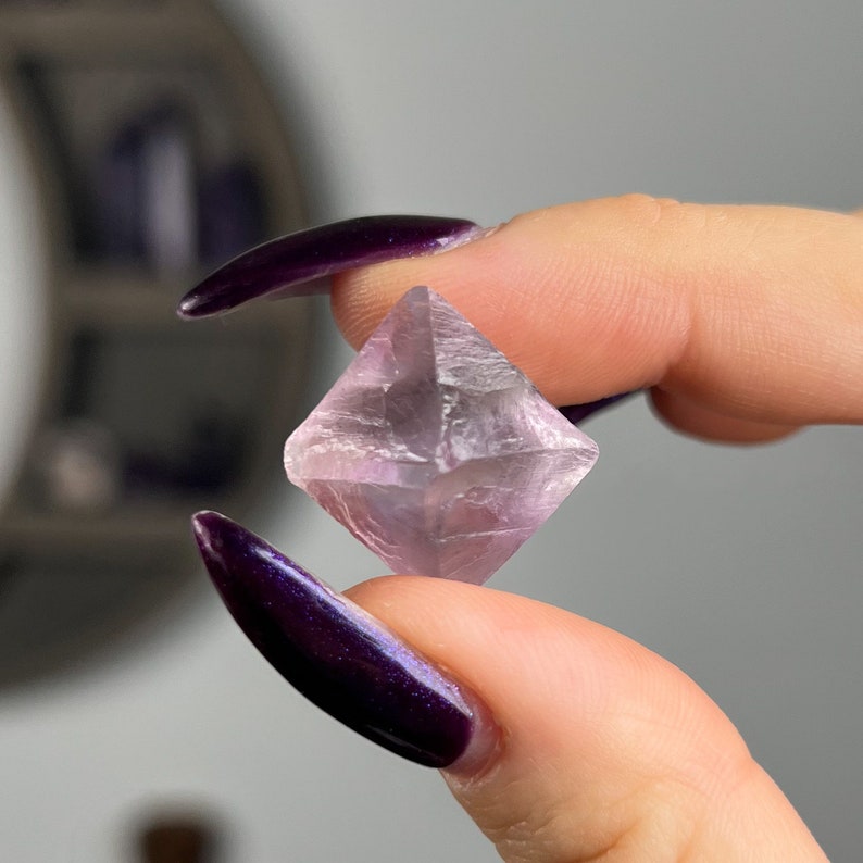 May include: A pink fluorite crystal with a geometric shape. The crystal is clear and has a slight purple hue.