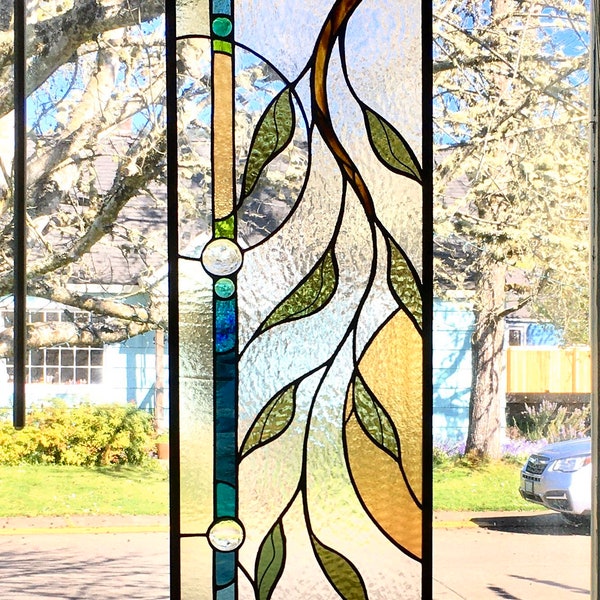 Stained glass window with vine, varied blue and green border and round shapes with amber opalescent glass.