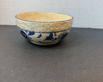 May include: A small, beige ceramic bowl with a blue floral design. The rim of the bowl is a darker blue, and the exterior has a textured, crackled appearance. The bowl is likely for serving or display.