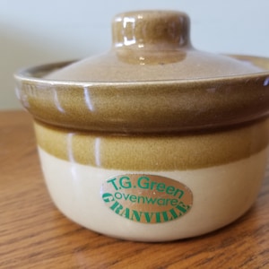 Puede incluir: Un plato para hornear de cerámica marrón y beige con tapa. El plato tiene una etiqueta verde que dice "T.G. Green Ovenware Granville".